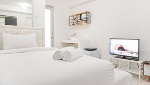 A hotel room with a bed, a television, a small table, and a shelf with items.