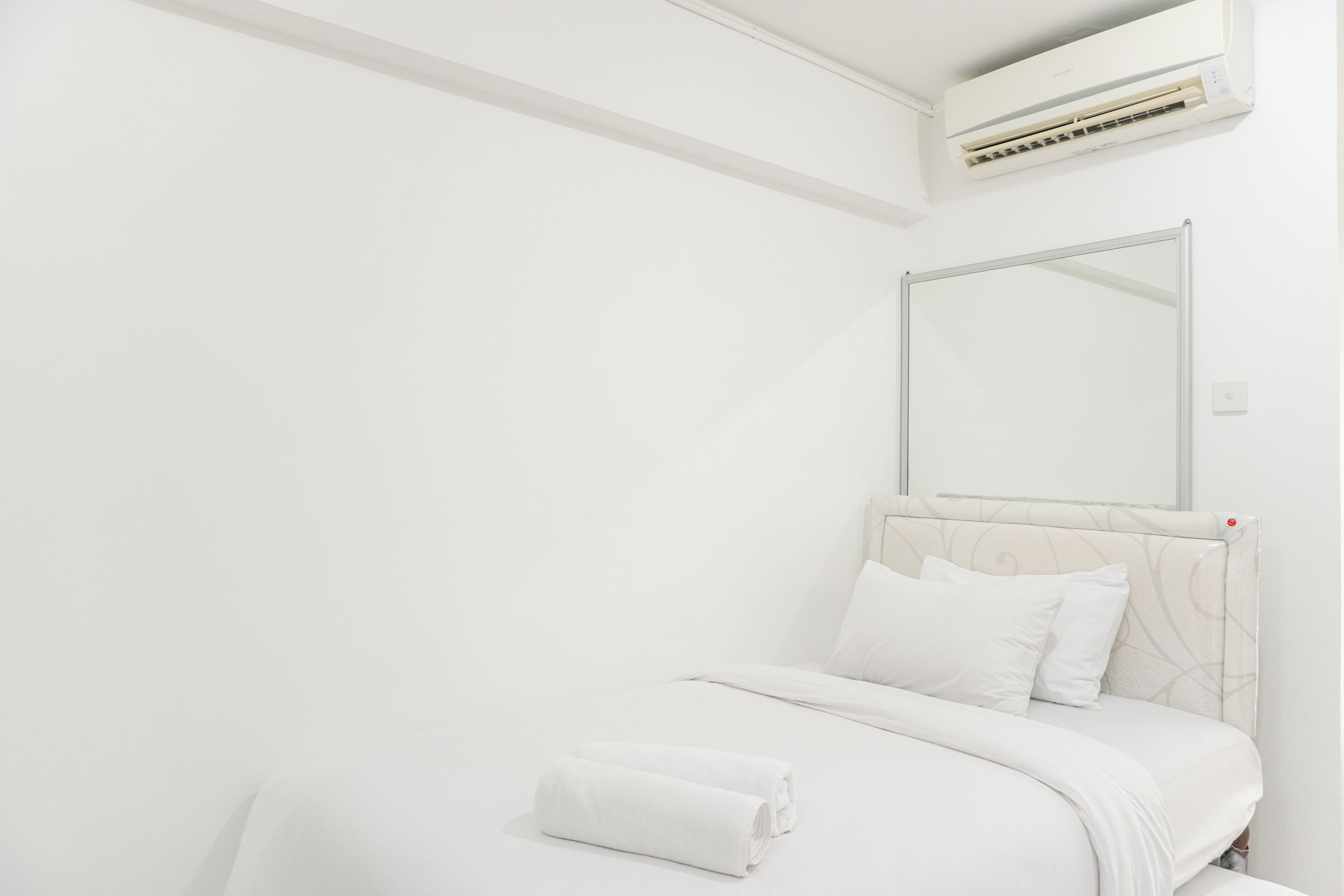 A minimalist hotel room with a bed, a large mirror, and an air conditioning unit.