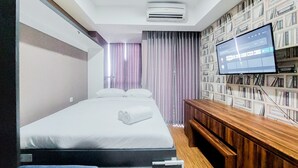 A hotel room with a bed, a TV, a bookshelf, and a wooden bench. - Modern Look Studio Pacific Garden Alam Sutera Apartment (Tangerang)