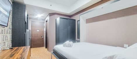 Una habitación de hotel moderna con un escritorio de madera, una cama con ropa blanca, un televisor de pantalla plana y una estantería.