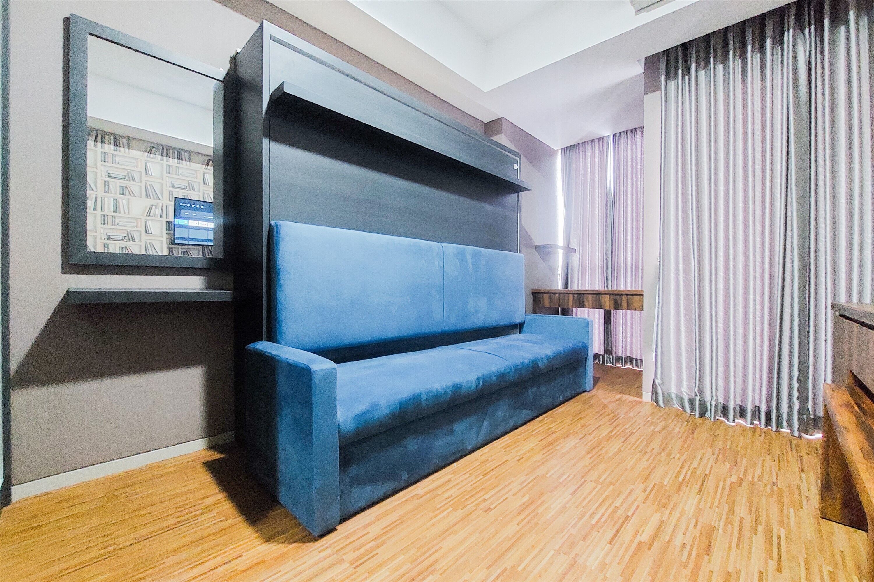 Une pièce moderne avec un canapé bleu, une bibliothèque et une grande fenêtre avec des rideaux.