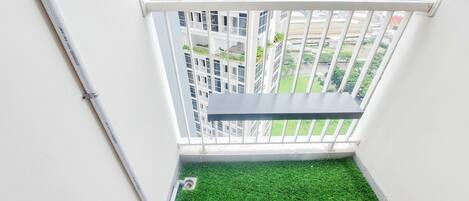 A small balcony with artificial grass, white railing, and a view of a high-rise building.
