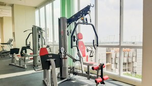 Un gimnasio con equipamiento de ejercicio, ventanas amplias y vistas a la ciudad.