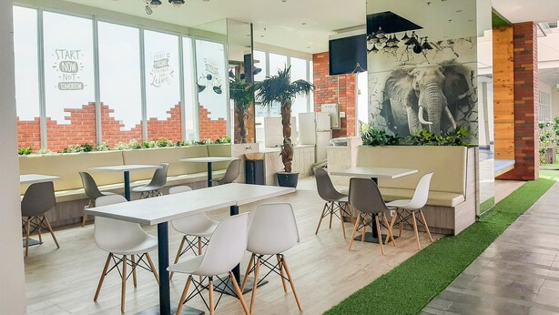 Un restaurante moderno con mesas y sillas blancas, un mural de un elefante y frases motivacionales en las ventanas.