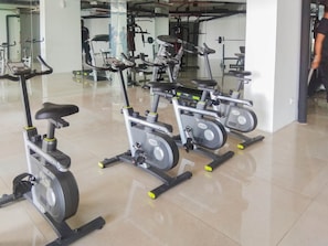 Une salle de sport équipée de vélos d’appartement, de machines de musculation et d’un mur recouvert de miroirs.