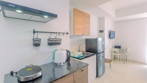 A compact kitchen with a Rinnai range hood, a kettle, a coffee maker, a refrigerator, and a dining area with a table and chairs.