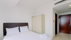 A hotel room with a neatly made bed, a wardrobe, and a door. - Cozy And Warm Studio At West Vista Apartment (Jakarta)