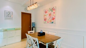 A dining area with a wooden table and white chairs, a water dispenser, and a clock on the wall. - Comfort Living 3Br Apartment At 25Th Floor Thamrin Residence (Jakarta)