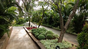 A pathway flanked by lush greenery and palm trees, leading to a seating area with red flowers. - Comfort Living 3Br Apartment At 25Th Floor Thamrin Residence (Jakarta)