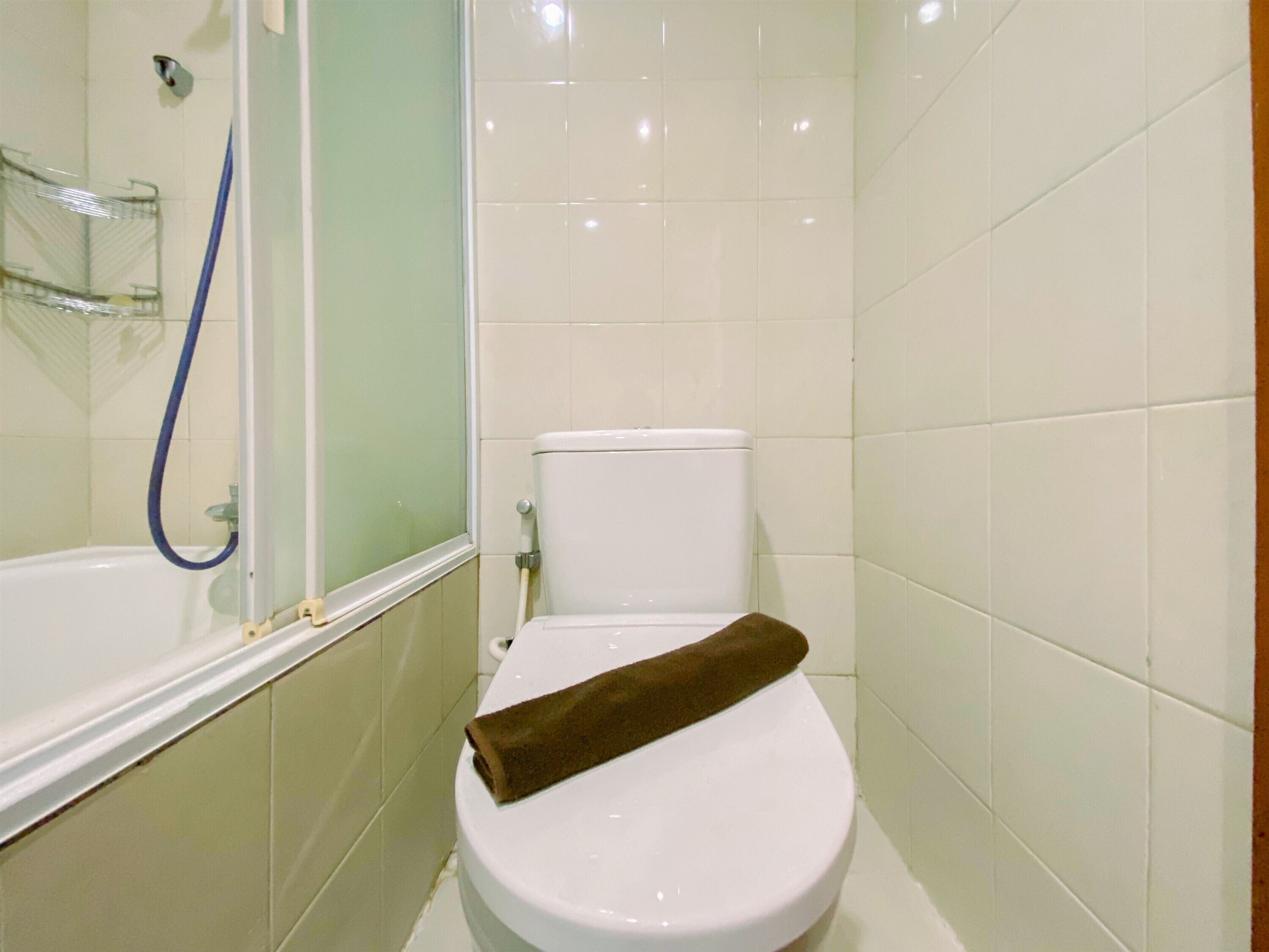 A bathroom with a white toilet, a shower with a blue hose, and a towel on the toilet.
