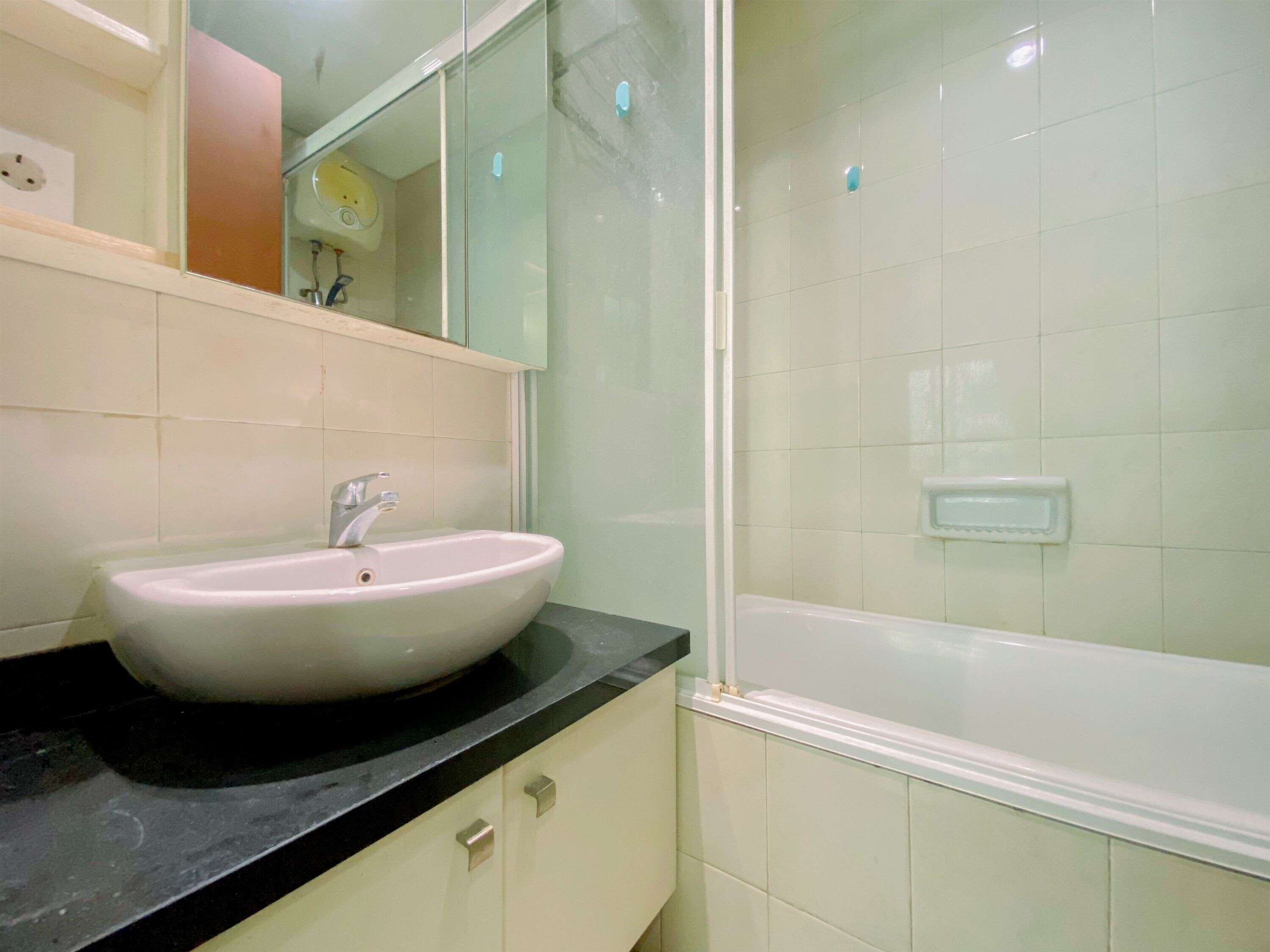 Un baño con lavamanos blanco, un espejo y zona de ducha.