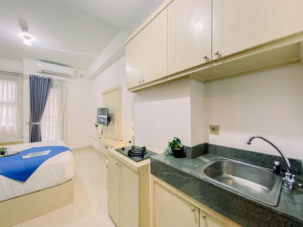 Cocina compacta con lavamanos, encimera, armarios y cama con colcha azul y blanca.