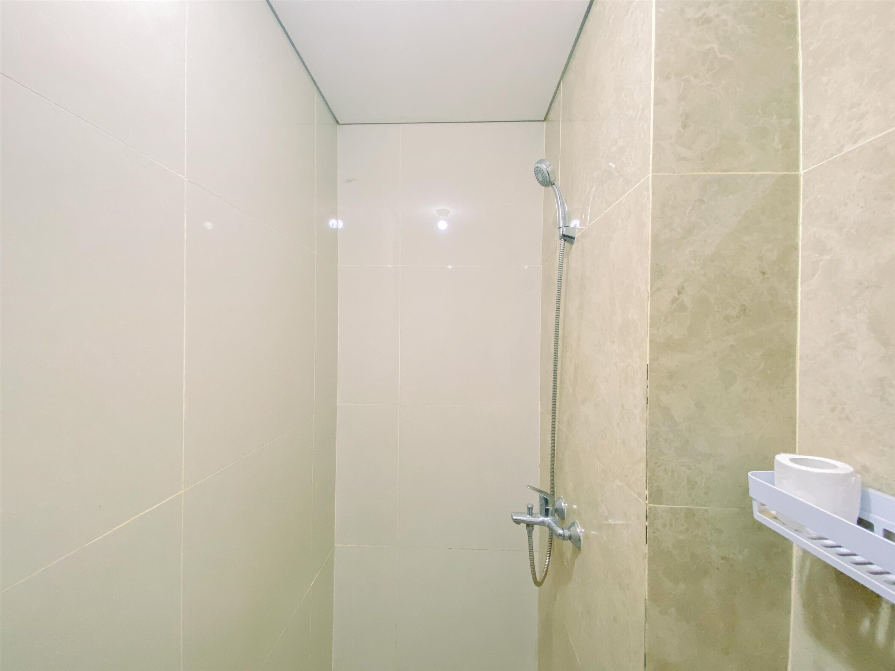 A small, tiled shower room with a handheld showerhead and a wall-mounted faucet.