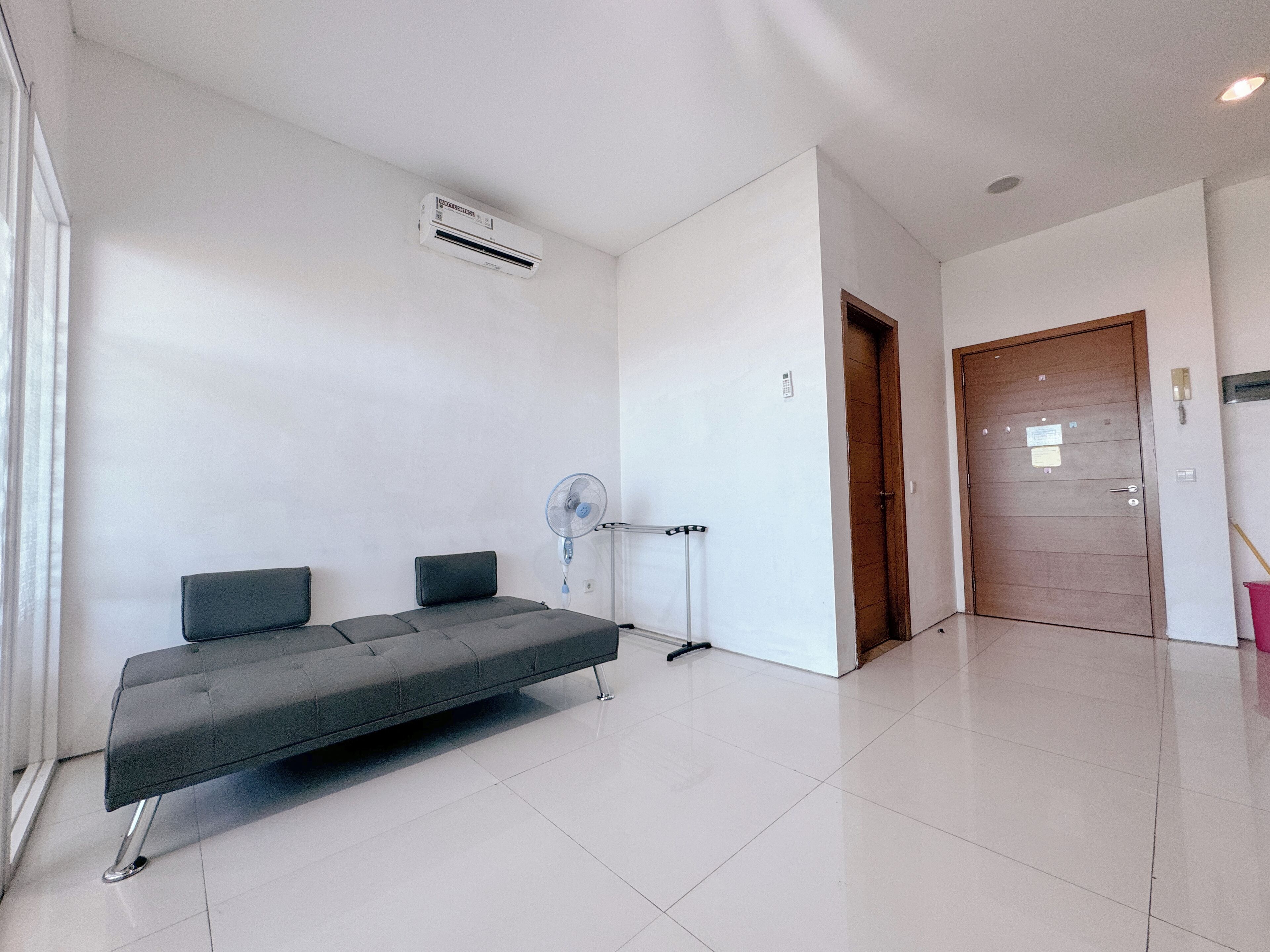 A modern hotel room with a sofa, a standing fan, and a wooden door.
