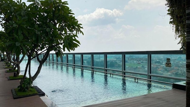Ein Infinity-Pool auf dem Dach mit Glasabschirmung, umgeben von Bäumen und einer Holzterrasse.