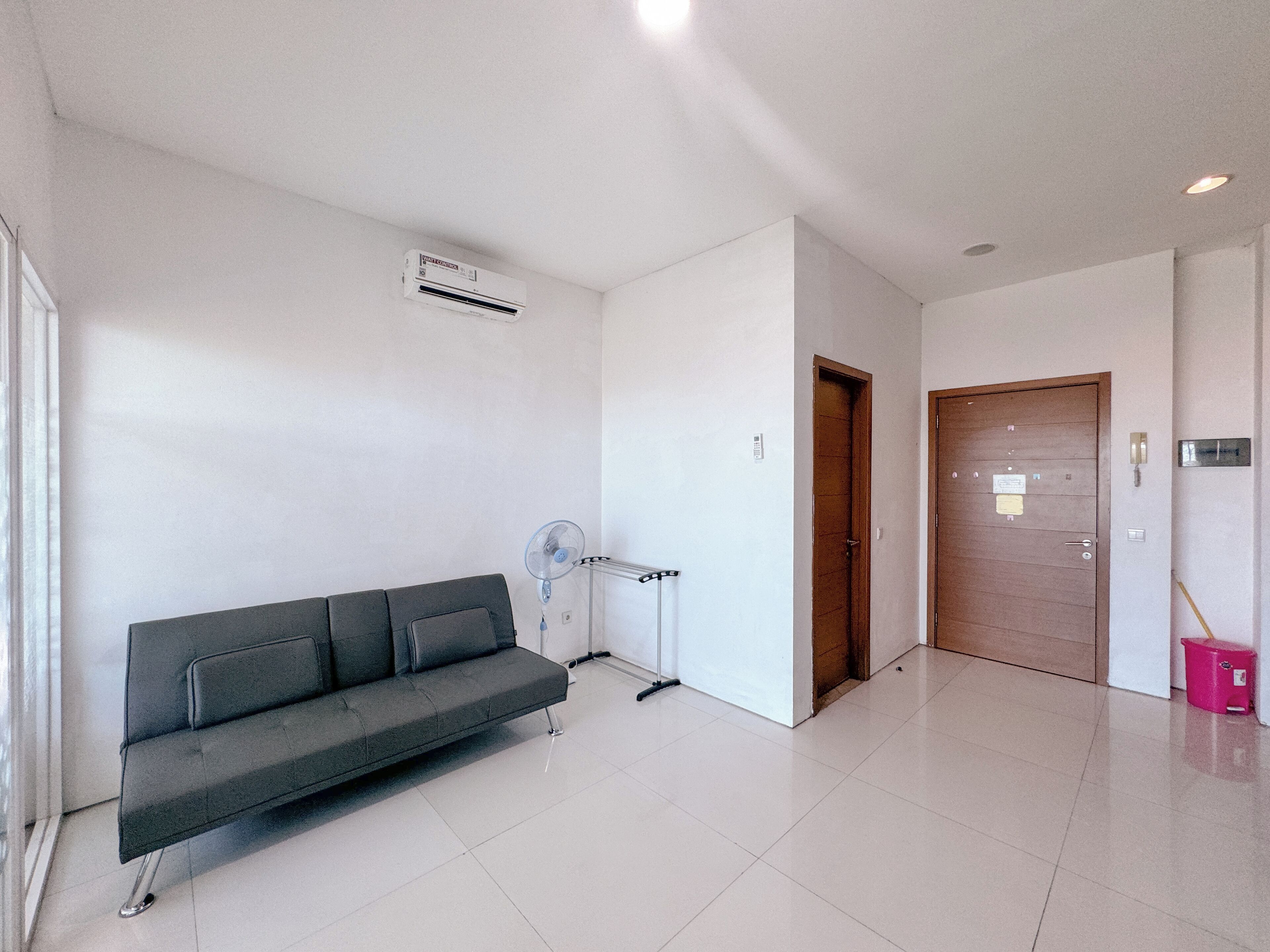 A modern interior with a grey sofa, a standing fan, a wooden door, and a tiled floor.