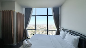 Ein Hotelzimmer mit einem großen Bett, Blick auf eine Stadtlandschaft und einem Vorhangfenster.