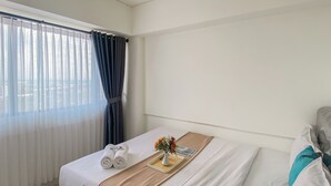 A hotel room with a bed, a window with sheer curtains, a tray with a vase of flowers, and a towel on the bed.