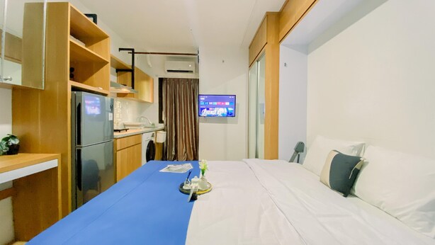 Ein kompaktes Hotelzimmer mit Küchenzeile, einem Bett, einem Fernseher und einem kleinen Tisch mit blauer Tischdecke.