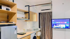 Eine kompakte Küche mit Waschmaschine, Kühlschrank und einem an der Wand befestigten Fernseher.