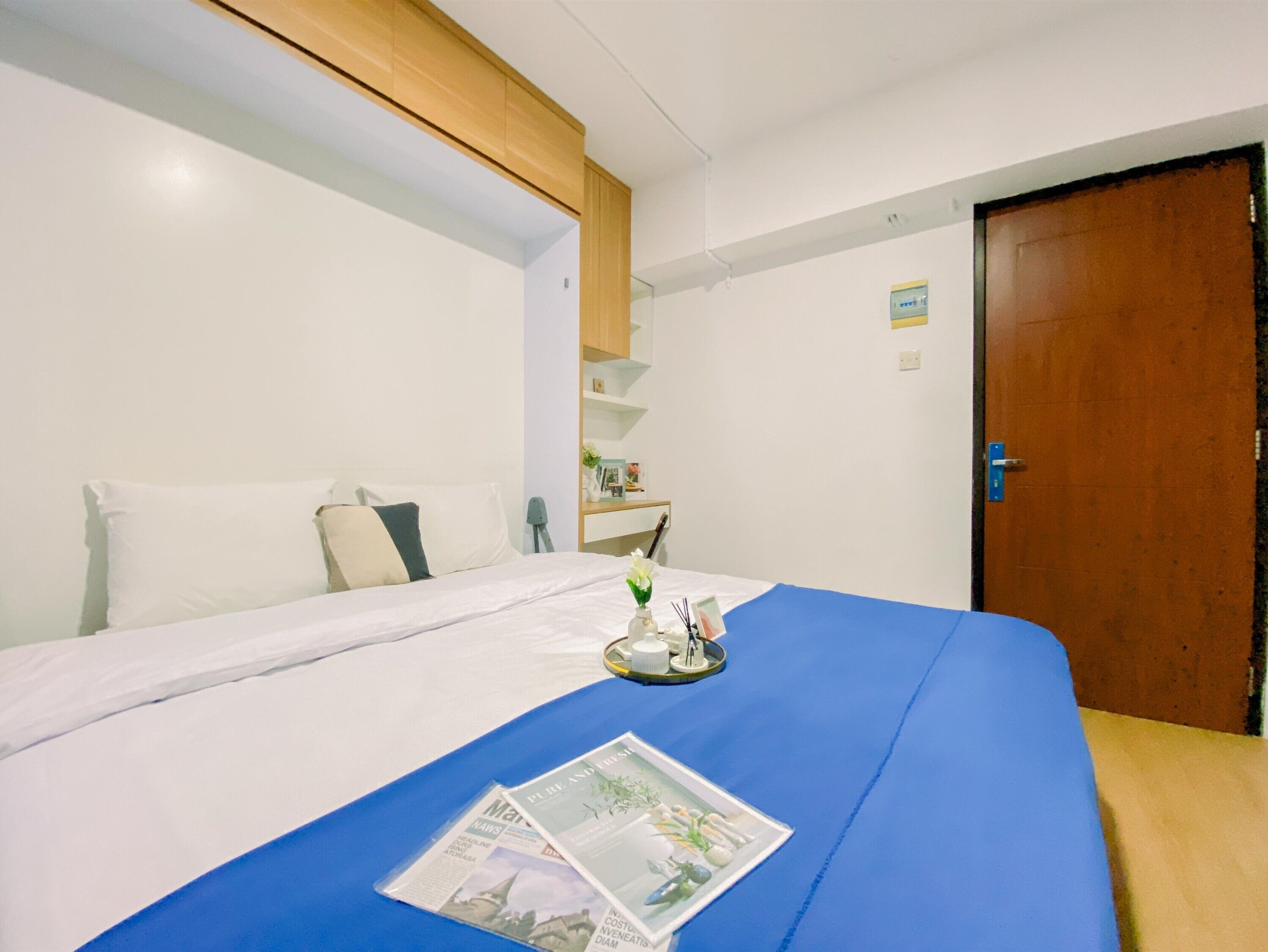 Une chambre d’hôtel avec un lit, une tête de lit en bois, un petit bureau et une porte.