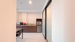 A modern kitchen with a refrigerator, microwave, and kettle. There is a dining table with chairs and a glass door leading to another room. - 2BR Apartment at Skales Residence Near Nusa Dua Square (Nusa Dua)