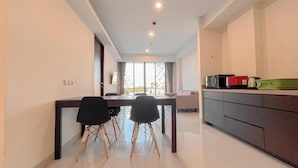A modern kitchen with a dining area, featuring a large window, a microwave, and a kettle on the counter. - 2BR Apartment at Skales Residence Near Nusa Dua Square (Nusa Dua)