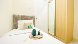 A neatly made bed with a white duvet, a blue flower in a green vase, and a tray with a bottle and a spoon. - Good Choice And Restful 2Br Green Pramuka City Apartment Near Mall (Jakarta)