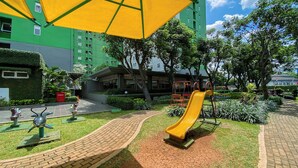 A playground with a yellow slide and exercise equipment, surrounded by green grass and trees. - Good Choice And Restful 2Br Green Pramuka City Apartment Near Mall (Jakarta)