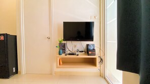 A compact living space with a television mounted on a wall, a small shelf with a plant, and a travel bag. - Good Choice And Restful 2Br Green Pramuka City Apartment Near Mall (Jakarta)