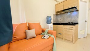 A compact living space with a sofa, a water dispenser, a kitchen area with cabinets and a sink, and a door. - Good Choice And Restful 2Br Green Pramuka City Apartment Near Mall (Jakarta)
