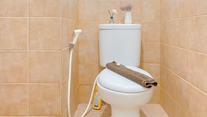A toilet with a brown towel on the seat, a bottle of toilet cleaner, and a vase with flowers on the tank.