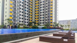 A high-rise residential building with balconies, a swimming pool, and outdoor seating.