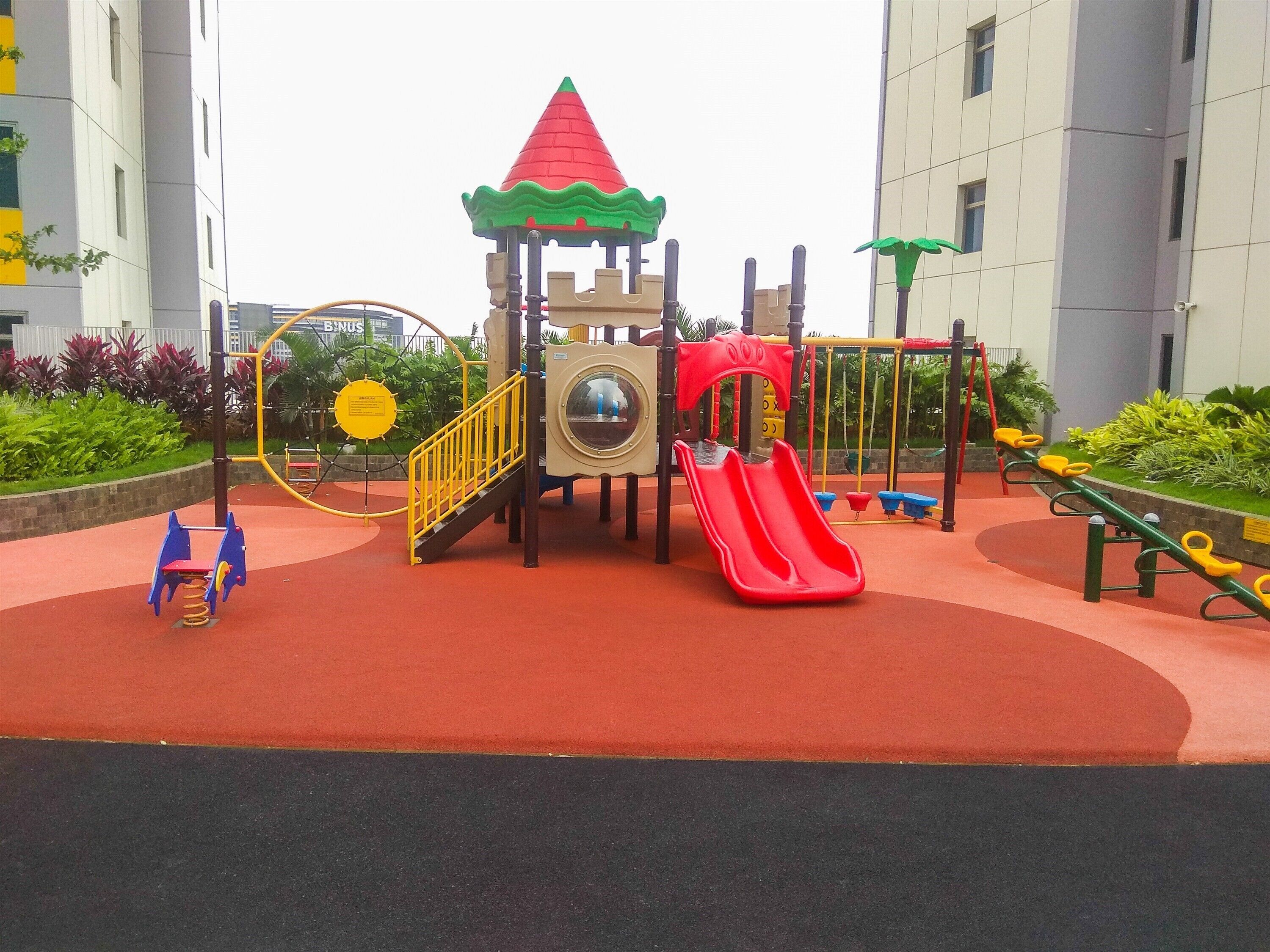 Un parque infantil con un tobogán rojo, estructuras para escalar y un columpio amarillo circular.