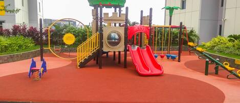 Un parque infantil con un tobogán rojo, estructuras para escalar y un columpio amarillo circular.
