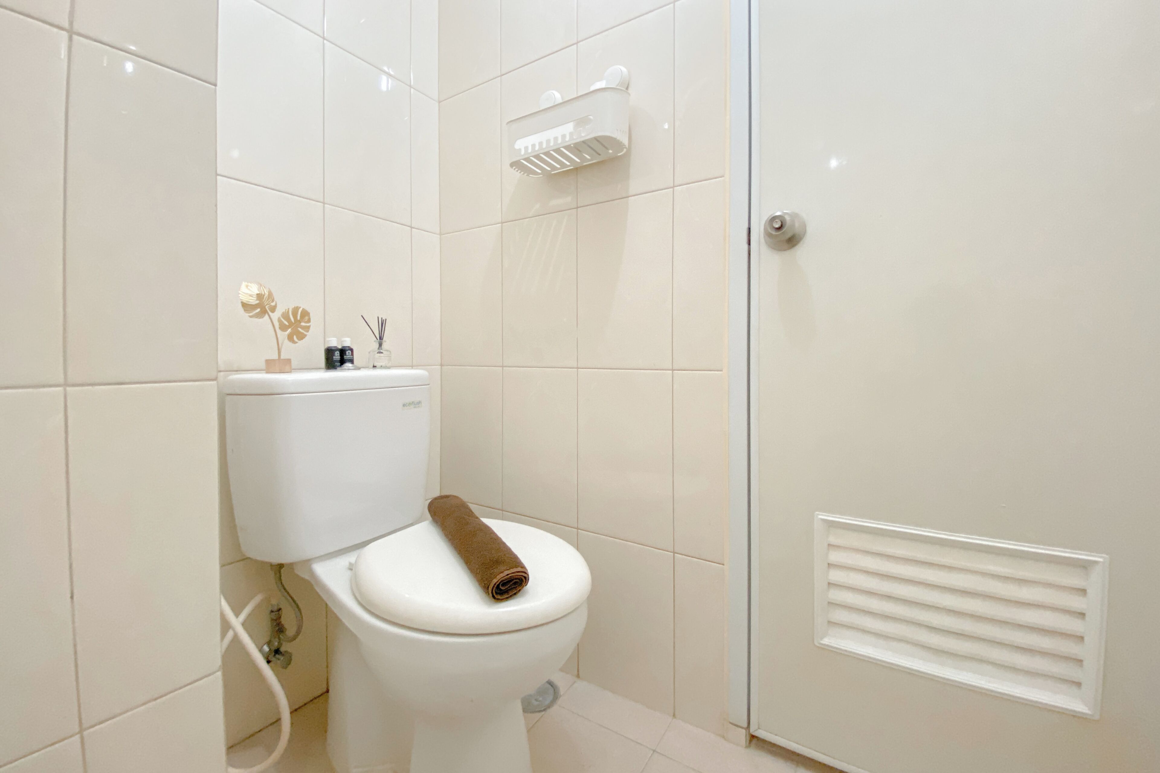 A bathroom with a toilet, a towel, a showerhead, and a vent.