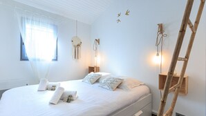 Un lit bien fait, avec du linge de lit et des serviettes blanches, une échelle en bois appuyée contre le mur et une petite table de chevet avec une lampe.