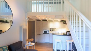 Une cuisine moderne dotée d’un îlot central, de tabourets de bar blancs et d’un escalier menant à un niveau supérieur.