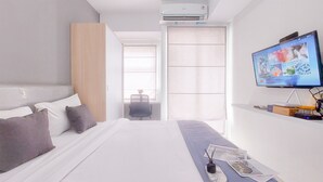 Quarto de hotel moderno com uma cama grande, televisão de tela plana, escrivaninha com cadeira e janela com persianas.