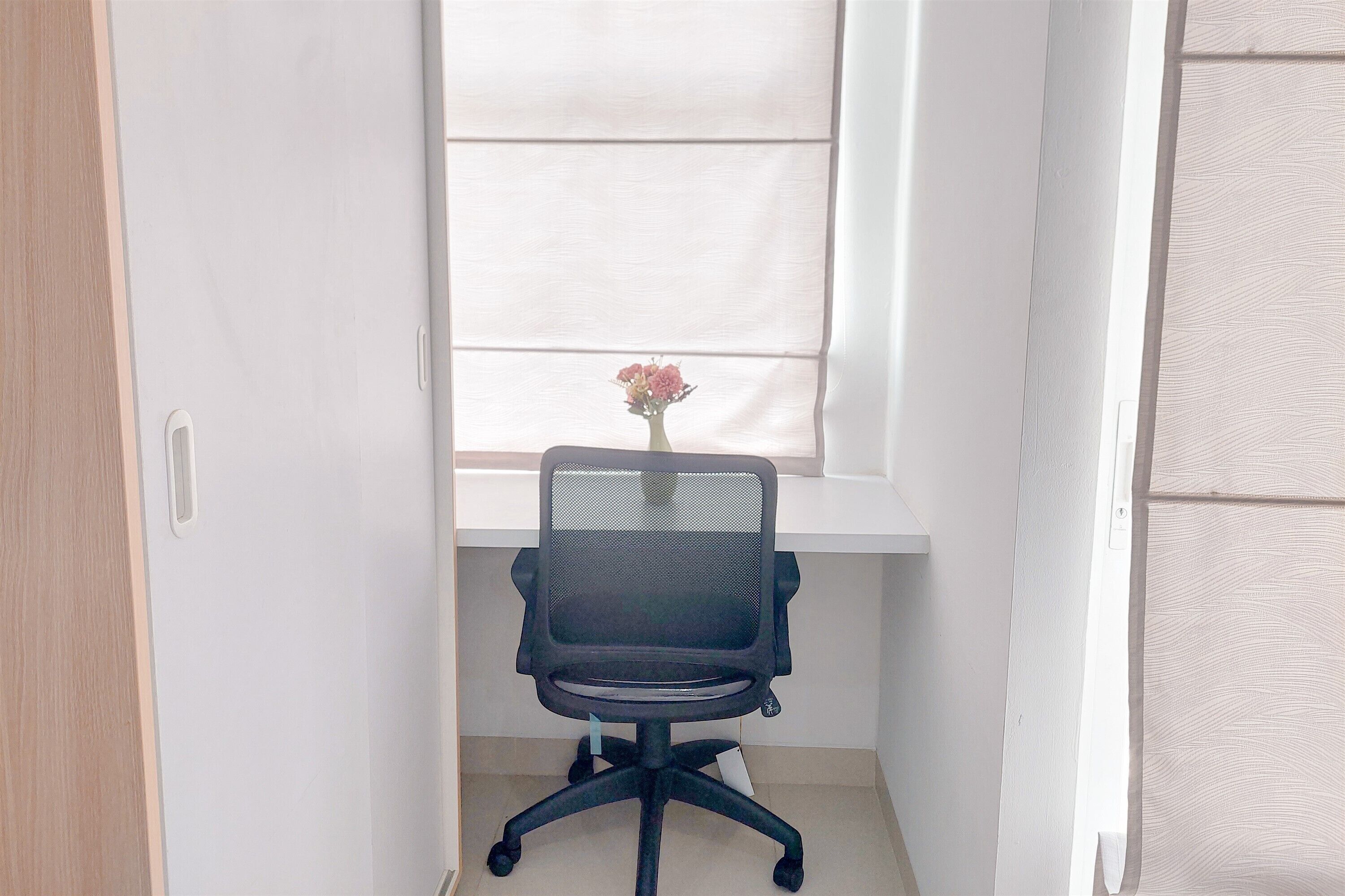 A small office space with a black office chair, a white desk, and a window with blinds.