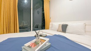 Habitación de hotel con una cama, ventana con cortinas, un reloj en la pared y un libro sobre la cama.