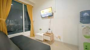 Habitación de hotel con cama, una mesita de noche con un florero, televisor montado en la pared y dispensador de agua.