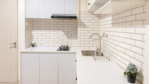 Una cocina compacta con armarios blancos, un salpicadero azulejado, un lavamanos y una pequeña estufa.