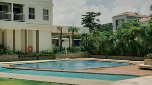Une piscine entourée d’un jardin aménagé, agrémenté de palmiers, et un bâtiment doté d’un balcon.