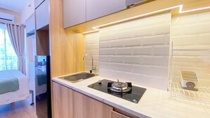 Une cuisine moderne et compacte, dotée d’un évier en acier inoxydable, d’une cuisinière à gaz et d’un dosseret de carrelage blanc.