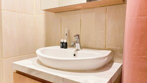 Un lavabo de salle de bain avec un plan de toilette en marbre, un miroir au-dessus et deux flacons de savon pour les mains placés sur le bord du lavabo.
