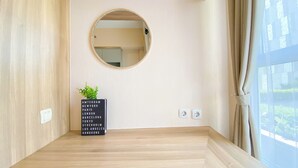 Une pièce avec un plancher en bois, un miroir rond accroché au mur, une petite plante en pot et une prise de courant.