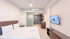 A hotel room with a bed, a TV on the wall, a kitchenette, and an air conditioning unit. - Studio Near Bali Collection Skales Residence Nusa Dua (Nusa Dua)