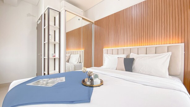A modern hotel room with a large bed, a wooden panel wall, a mirror, and a bedside table with a tray. - Cozy And Good Place 2Br Transpark Cibubur Apartment (Depok)