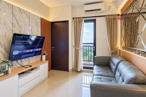 A modern living room with a flat-screen TV, a sofa, a wooden console table, and a door leading to a balcony. - Cozy And Good Place 2Br Transpark Cibubur Apartment (Depok)